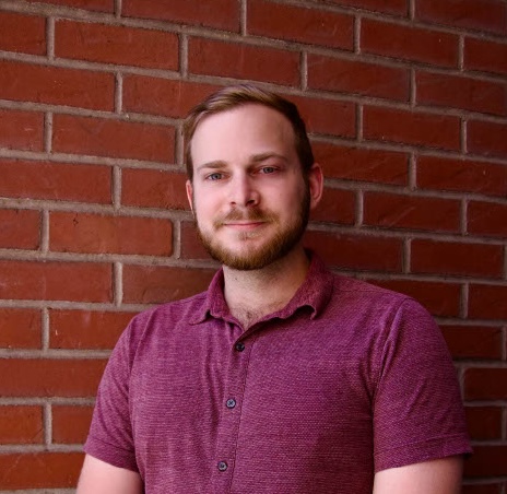 Moss, a white man with short blonde hair and a beard, smiles with his mouth closed.