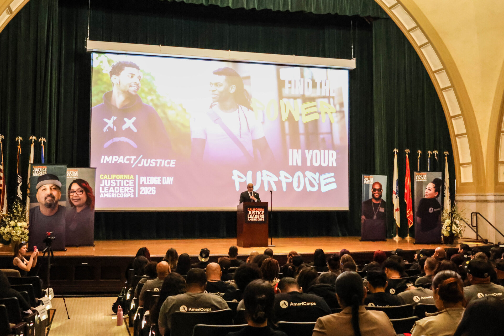 A large auditorium room filled with people; signage on the stage includes the California Justice Leaders logo and a banner reading "Find the power in your purpose."
