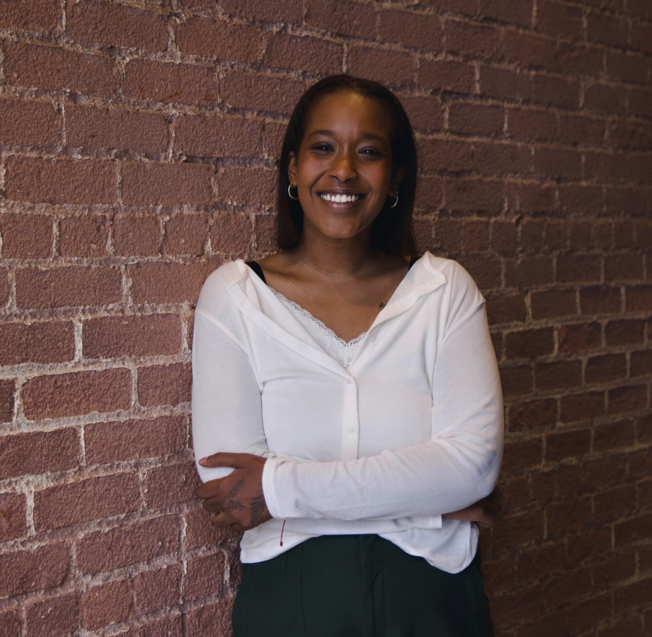 Hawa, a black woman with short dark brown hair, is smiling and wearing a white top