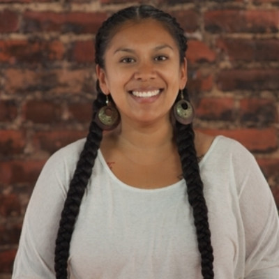 Darlene, a brown-skinned woman with boxer-type braids, smiling, and wearing a cream-colored shirt.