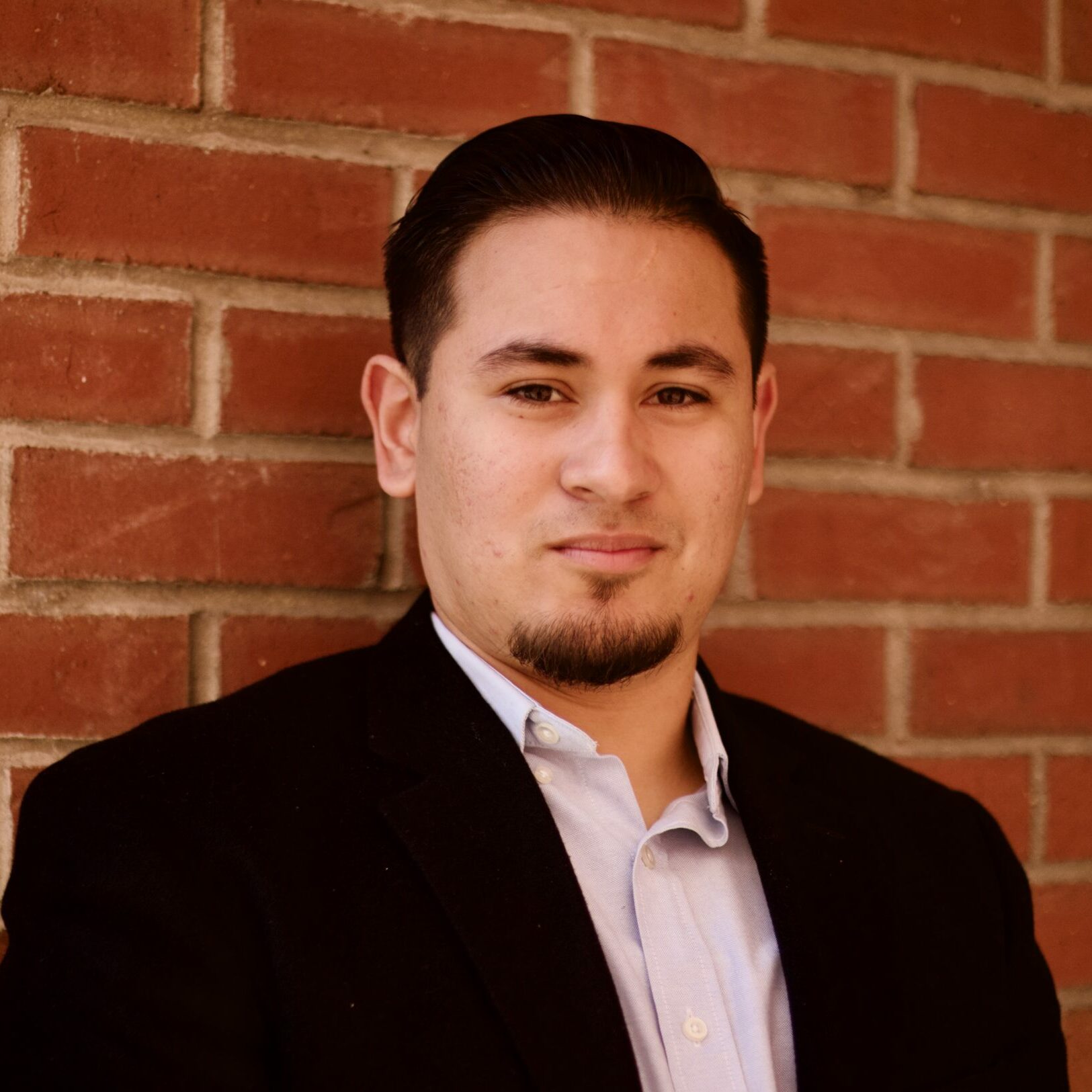 Ben, a Latino man with a combover, is standing in front of a brick wall.