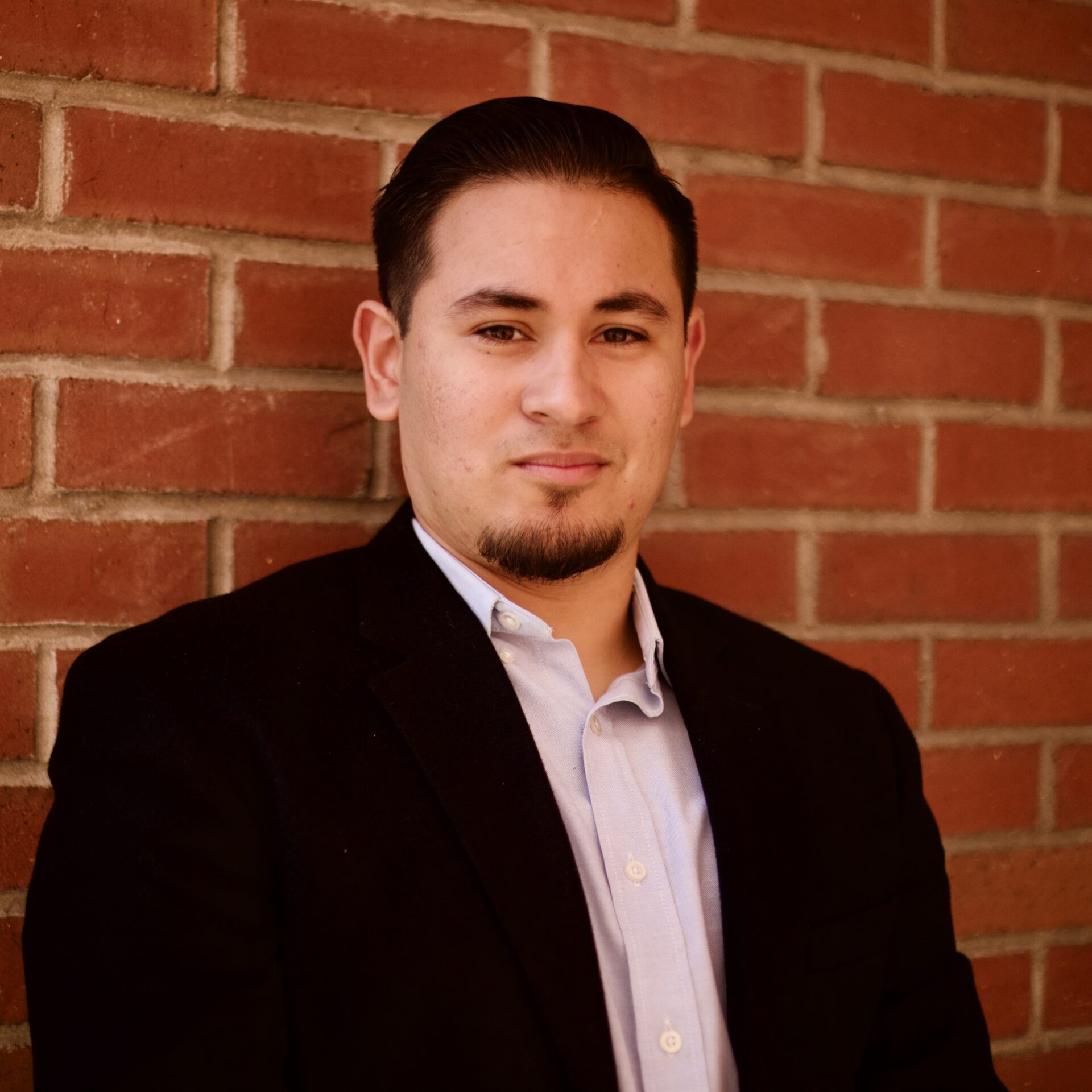 Ben, a Latino man with a combover, is standing in front of a brick wall.