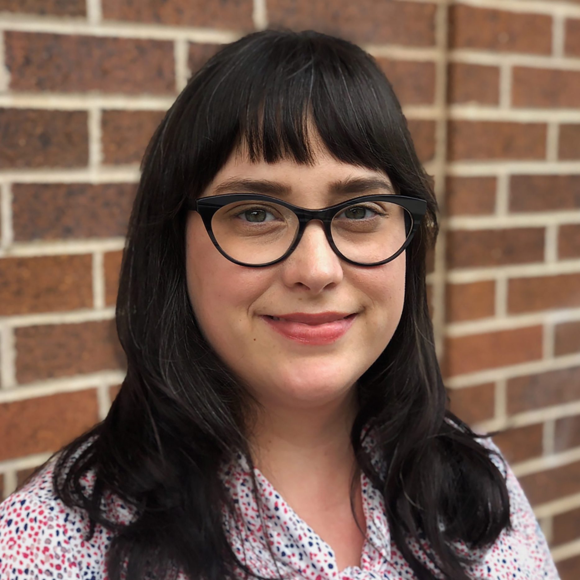 Erica, a dark-haired white female wearing dark-framed glasses, is wearing a floral blouse.