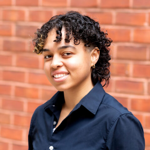 Briana, a hispanic woman with short curly hair, is smiling.