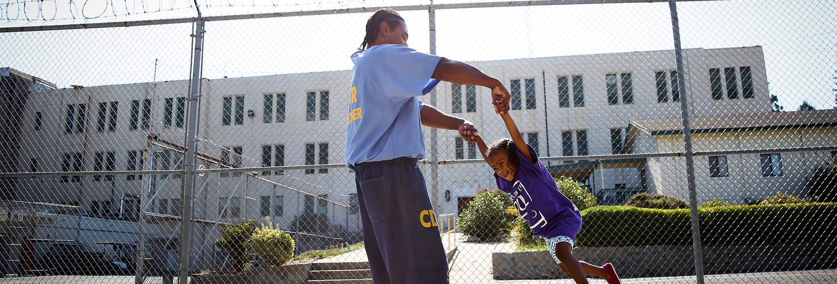 A man in a CDCR uniform swings a child by the arms, both are smiling.
