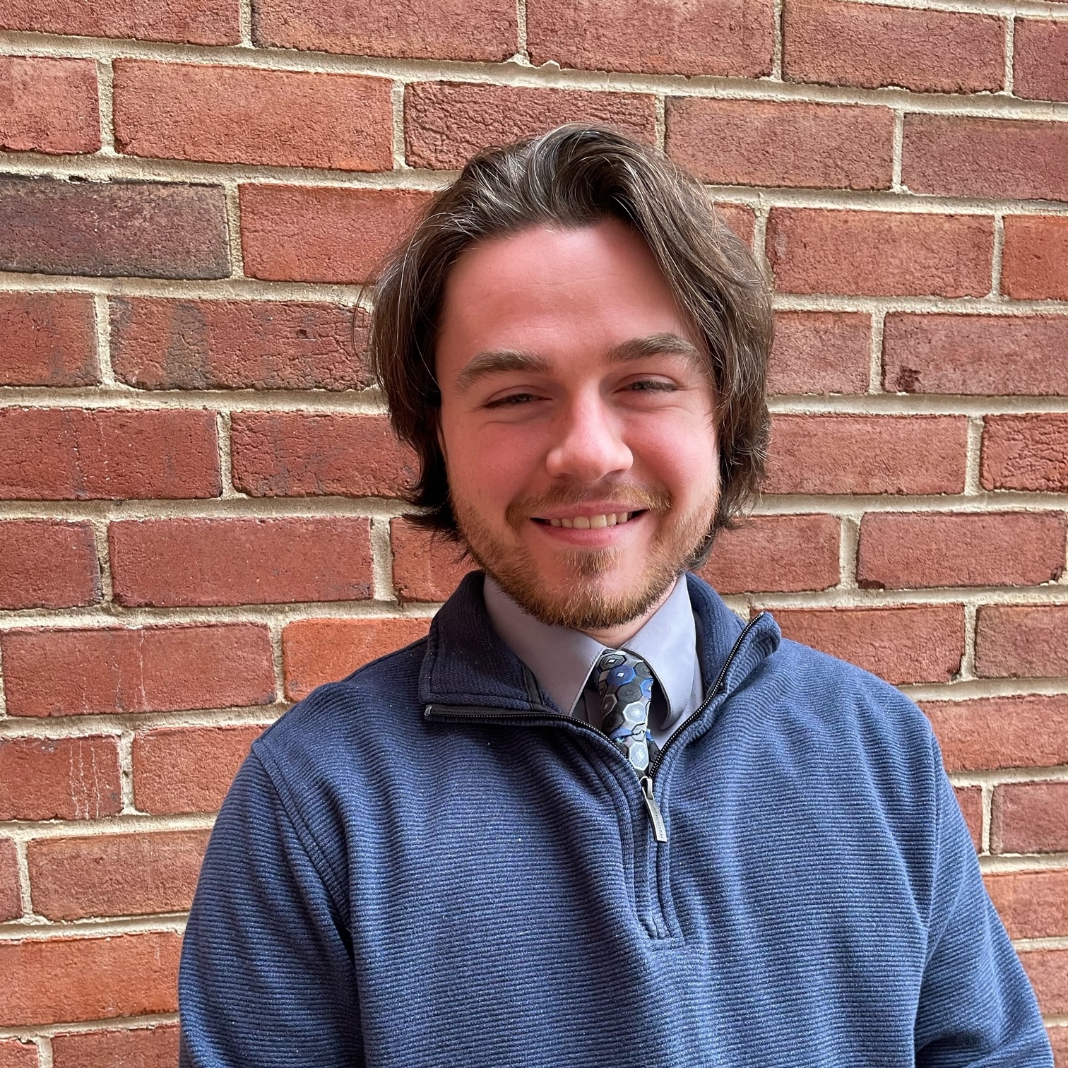 J.D., a white man with medium length brown hair and a short beard, smiling while wearing a blue sweater.