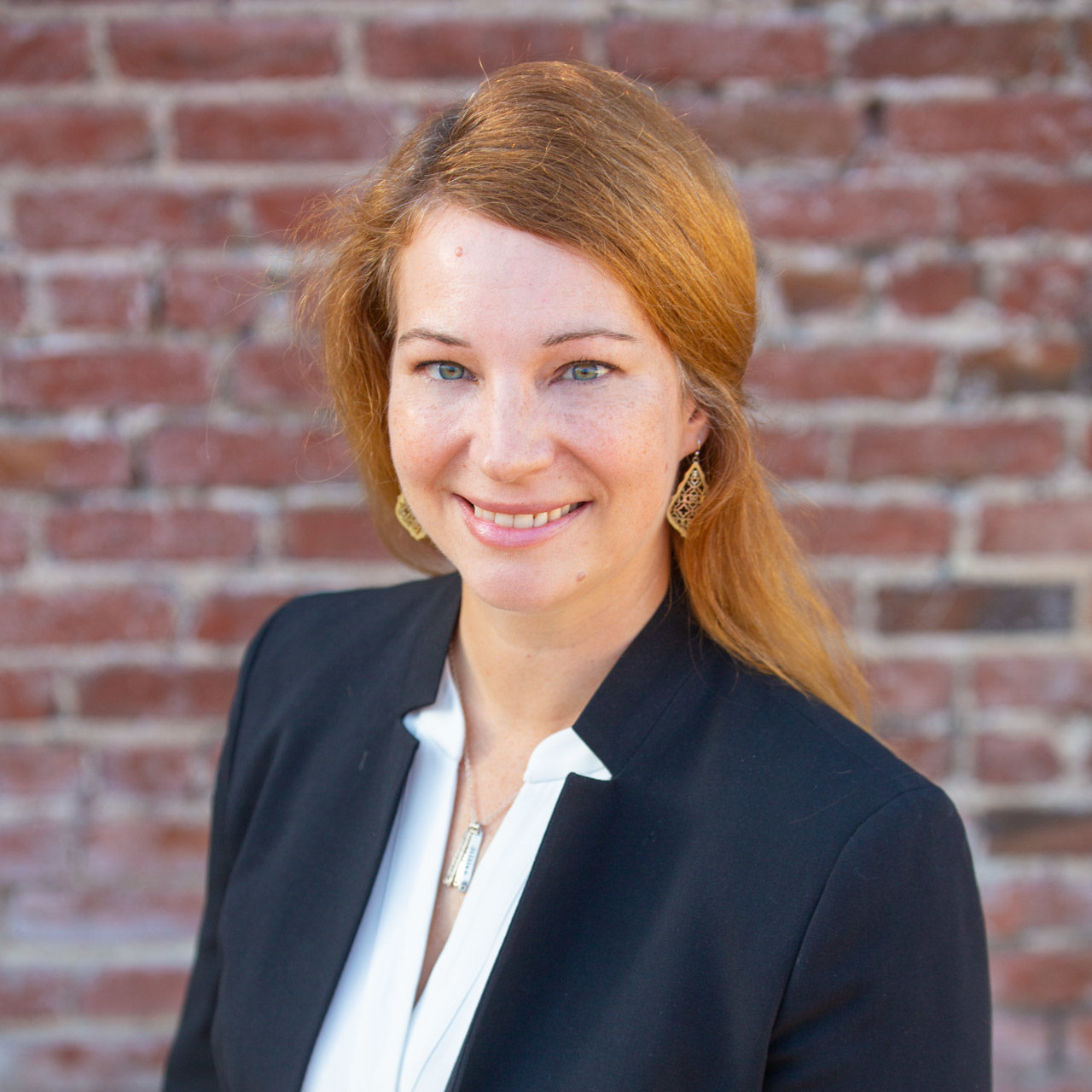 Michele, a white woman, is wearing a white shirt with a black jacket and smiling.