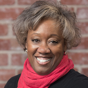 Marion, an African American woman is standing in front of a brick wall smiling broadly.